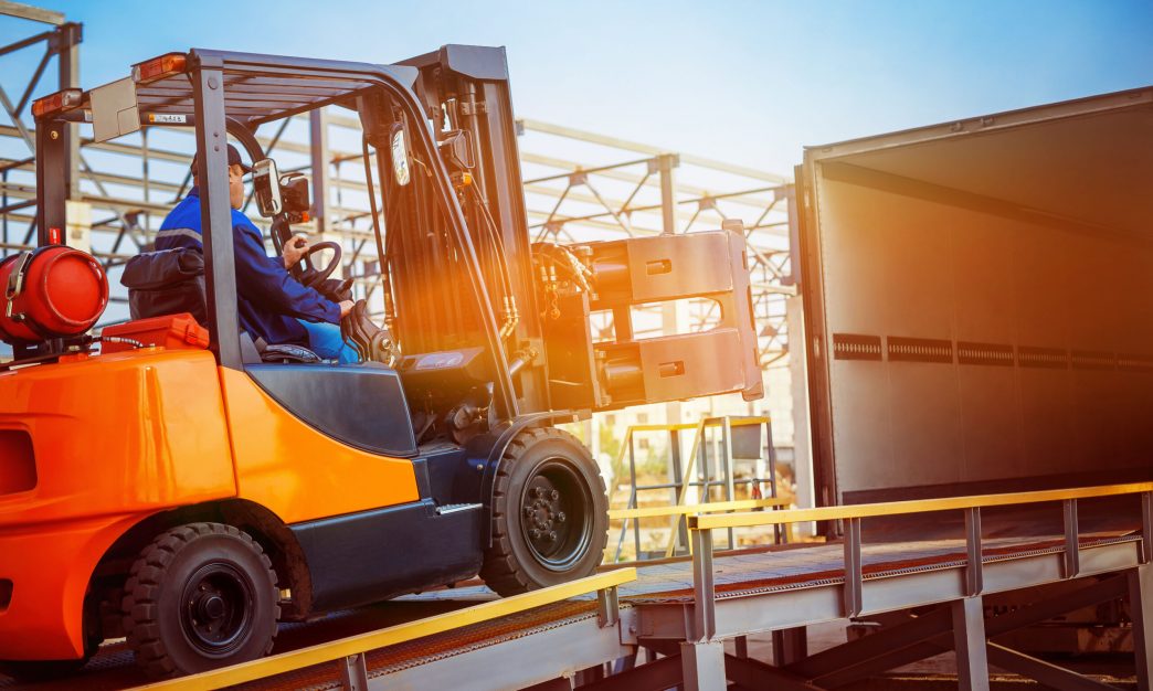 Forklift is putting cargo from warehouse to truck outdoors